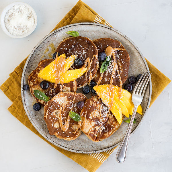 Fruit pancake platter with mango, blueberries, strawberry, and a coconut drizzle, perfect for Organic Desiccated Coconut recipes.