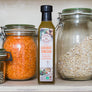 Bottle of Coconut Merchant Organic Coconut Vinegar with Turmeric and Moringa in a kitchen pantry next to glass jars of lentils